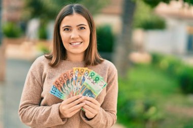 Genç İspanyol kadın gülümseyerek Avustralya dolarlarını şehirde tutuyor..