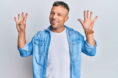 Yakışıklı, sıradan bir kot ceket giyen kaslı bir adam dokuz numaralı parmaklarını gösterip gösterirken kendinden emin ve mutlu bir şekilde gülümsüyor.. 