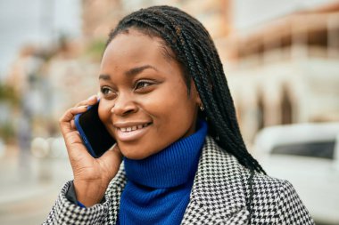 Genç afro-amerikan iş kadını gülümseyerek şehirdeki akıllı telefondan konuşuyor..