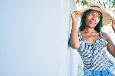 Genç Afro-Amerikan kadın tatilde gülümsüyor ve şehrin duvarına yaslanıyor.