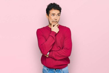 Gündelik kıyafetler giyen genç yakışıklı bir adam bir soru hakkında endişeli ve gergin bir şekilde düşünüyor. 