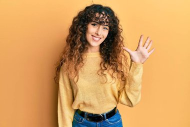 Gündelik kıyafetler giyen genç İspanyol kız beş numarayı gösterip işaret ederken kendinden emin ve mutlu gülümsüyor.. 