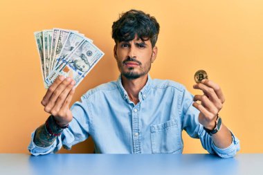 Genç İspanyol adam dolarları tutuyor ve bitcoin 'den bihaber ve kafası karışık bir ifade. şüphe kavramı. 