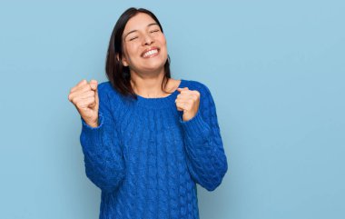 Gündelik kıyafetler giyen genç İspanyol kadın başarı için heyecanlı kolları havada ve gözleri kapalı zaferi kutlarken gülümsüyor. Kazanan konsept. 