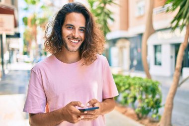 Genç İspanyol adam şehirde akıllı telefon kullanarak mutlu gülümsüyor..