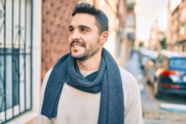 Şehre yürürken atkı takan, mutlu gülümseyen genç İspanyol adam..