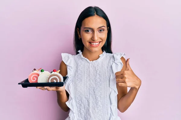 Mujer Morena Joven Sosteniendo Dulces Pastel Sonriendo Feliz Positivo Pulgar —  Fotos de Stock