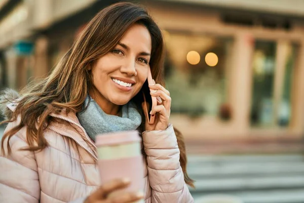 Genç İspanyol kadın gülümsüyor. Şehirdeki akıllı telefondan konuşuyor..