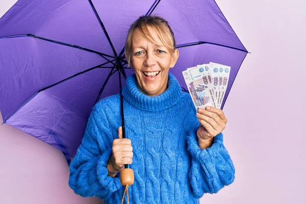 中世ブロンド女性保持傘とロシアのルーブル紙幣笑顔と笑いますハードアウト大声でなぜなら面白いクレイジー冗談 — ストック写真