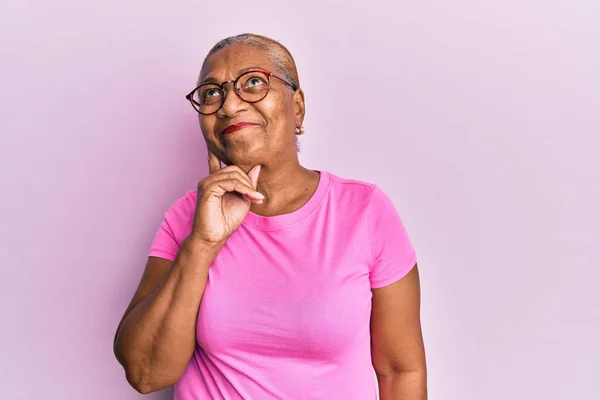Senior african american woman wearing casual clothes and glasses serious face thinking about question with hand on chin, thoughtful about confusing idea