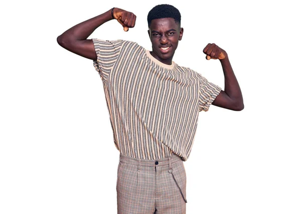若いアフリカ系アメリカ人の男性は腕の筋肉を示すカジュアルな服を着て誇らしげに笑っている フィットネスのコンセプト — ストック写真