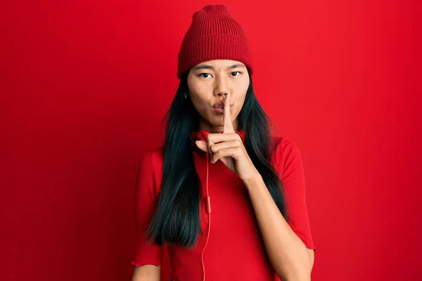 年轻的中国女人用耳机听音乐 要求保持安静 手指放在嘴唇上 沉默和秘密概念 — 图库照片