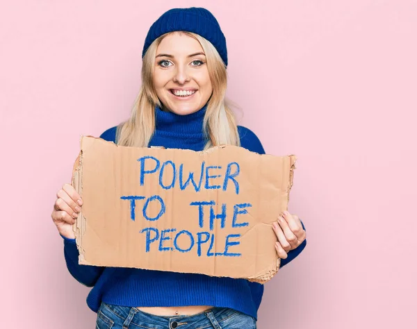 Young caucasian woman holding power to the people banner looking positive and happy standing and smiling with a confident smile showing teeth