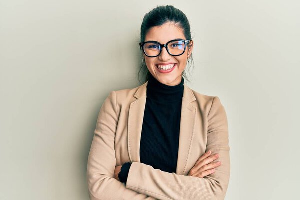 Young hispanic woman wearing business style and glasses happy face smiling with crossed arms looking at the camera. positive person. 