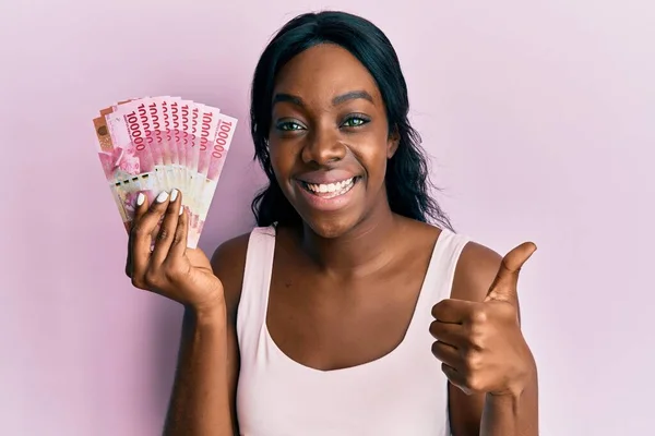 Joven Mujer Afroamericana Sosteniendo Billetes Rupias Indonesias Sonriendo Feliz Positivo — Foto de Stock