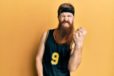 Kızıl saçlı, uzun sakallı, basketbol üniforması giyen kızgın, kızgın yumruğunu kaldıran öfkeli ve öfkeyle bağıran bir adam. öfke ve agresif konsept. 