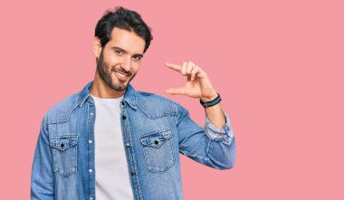 Gündelik kıyafetler giyen, gülümseyen, kendine güvenen, el hareketi yapan, parmaklarıyla işaret yapan ve kameraya bakan genç İspanyol bir adam. ölçüm kavramı. 