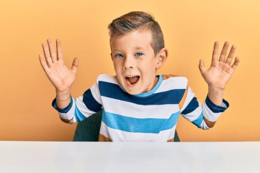 Sevimli beyaz çocuk, gündelik giysiler içinde masada oturmuş çılgınlığı kutluyor ve başarıya hayret ediyor. Kolları havada ve gözleri açık, heyecanlı bir şekilde çığlık atıyor. Kazanan konsept 