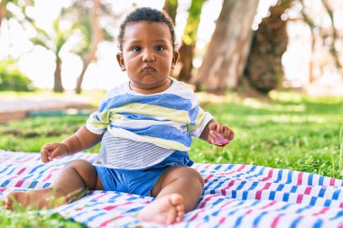 Sevimli Afro-Amerikan çocuk parkta çimlerin üzerinde oturuyor..