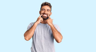 Gündelik kıyafetler giymiş, ağzı açık gülümseyen, parmakları işaret eden ve neşeli gülümsemeye zorlayan genç İspanyol bir adam. 