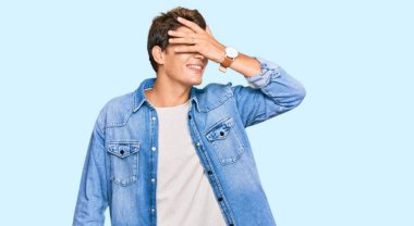 Sıradan bir kot ceket giyen yakışıklı beyaz adam. Gülümsüyor ve elleri yüzünde, şaşırmak için gözlerini kapatıyor. kör kavram. 