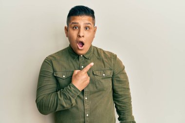 Gündelik kıyafetler giyen genç latin adam parmaklarını yana doğru göstererek şaşırdı, ağzı açık hayret içinde kaldı.. 