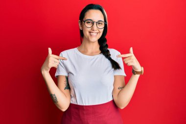 Genç İspanyol kadın profesyonel garson önlüğü giyiyor. Yüzünde bir gülümsemeyle kendinden emin görünüyor. Kendini gururlu ve mutlu olarak gösteriyor.. 