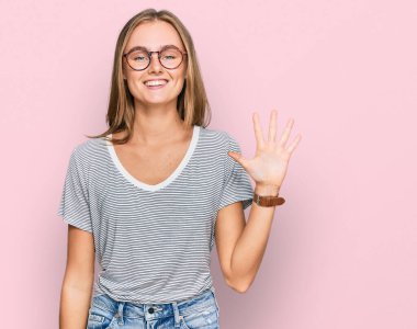 Güzel, genç, sarışın bir kadın. Günlük kıyafetler ve gözlük takıyor. Beş numaralı parmaklarıyla gösteriyor ve işaret ediyor.. 