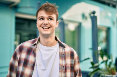 Genç beyaz adam gülümseyerek şehirde mutlu mesut duruyor..