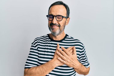 Orta yaşlı İspanyol bir adam gündelik kıyafetler ve gözlük takıyor elleri göğsünde gülümsüyor, gözleri kapalı ve yüzünde minnet dolu bir jest var. sağlık kavramı. 