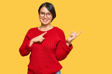 Kısa saçlı, sıradan bir süveter giyen, gözlüklü, gülümseyen ve kameraya bakan genç, güzel İspanyol bir kadın. İki eliyle ve parmaklarıyla onu işaret ediyor.. 