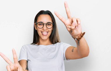 Latin kökenli genç bir kadın, günlük beyaz tişörtler giyip iki elini de göstererek gülümseyerek zafer işareti yapıyor. İki numara.. 