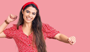 Esmer genç kız yaz elbisesi giymiş mutlu ve neşeli dans ediyor, gülümsüyor rahat ve kendinden emin bir şekilde müzik dinliyor. 