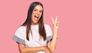 Gündelik kıyafetler giyen, gülümseyen, kameraya göz kırpan genç İspanyol kadın zafer işareti yapıyor. İki numara.. 