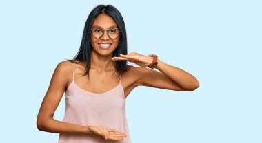 Genç Afrikalı Amerikalı kadın gündelik kıyafetler ve gözlük takıyor. Büyük ve büyük beden işareti gösteren el kol hareketleri yapıyor. Ölçüm sembolü. Kameraya bakıp gülümsüyor. ölçüm kavramı. 