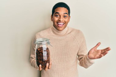 Genç, yakışıklı, elinde kuru üzümlerle dolu bir kavanoz tutan yakışıklı adam başarıyı mutlu bir gülümsemeyle kutluyor ve kazanan yüz ifadesini kaldırıyor. 