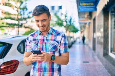 Beyaz adam şehirde akıllı telefon kullanarak mutlu bir şekilde gülümsüyor..