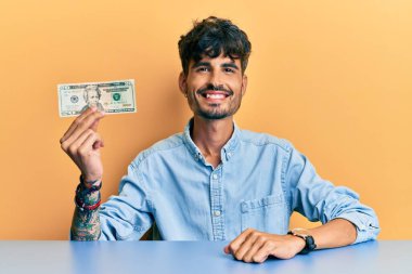 20 dolarlık banknot tutan genç İspanyol adam pozitif ve mutlu görünüyor ve kendine güvenen bir gülümsemeyle dişlerini gösteriyor. 