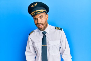 Sakallı, uçak pilotu üniforması giyen yakışıklı adam kameraya seksi bir ifadeyle bakıyor, neşeli ve mutlu bir yüzle.. 