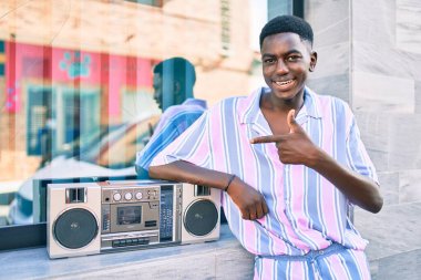 Genç Afrikalı Amerikalı adam duvara dayanmış teyp kullanarak müzik dinliyor..