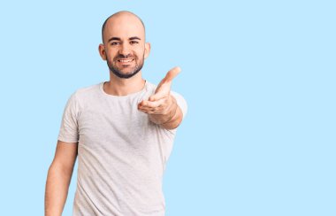 Gündelik tişört giyen genç yakışıklı adam dostça bir selamlama ve hoş geldin hediyesi olarak el sıkışmayı sunuyor. başarılı iş. 