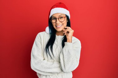Güzel İspanyol kadın Noel şapkası takıyor gülümsüyor kameraya kollarını kavuşturup ve çenesini kapatarak bakıyor. Olumlu düşünmek. 