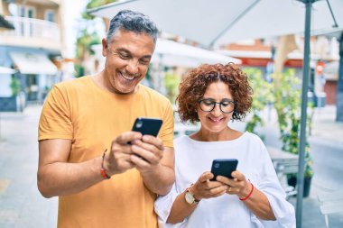 Şehrin caddesinde akıllı telefon kullanan orta yaşlı çift mutlu gülümsüyor..