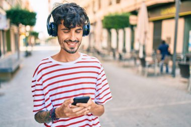 Şehrin caddesinde yürüyen, kulaklık ve akıllı telefon kullanan genç bir İspanyol..