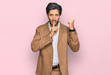 İş kıyafetleri giymiş genç İspanyol adam sessiz olmak istiyor. Parmakları dudaklarında, elleri yandan işaret ediyor. sessizlik ve gizli konsept. 