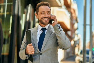 Orta yaşlı işadamı gülümsüyor. Şehirdeki akıllı telefondan konuşuyor..