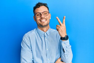 Gündelik kıyafetler giyen ve gözlüklü genç İspanyol adam kameraya gülümseyen gülen yüzle parmaklarıyla zafer işareti yapıyor. İki numara.. 
