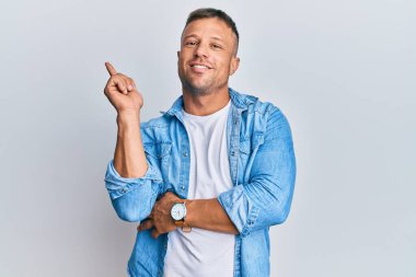 Yakışıklı, sıradan kot ceket giyen, yüzünde kocaman bir gülümseme olan, eli ve parmağı kameraya bakan kaslı bir adam.. 