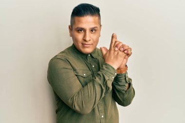 Gündelik kıyafetler giyen genç latin adam. Elinde sembolik bir silahla el hareketleriyle cinayet silahlarıyla oynuyor. Kızgın surat. 