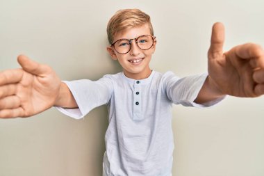 Sıradan kıyafetler ve gözlük takmış beyaz bir çocuk kameraya bakıp sarılmak için kollarını açmış gülümsüyor. Mutluluğu kucaklayan neşeli bir ifade.. 